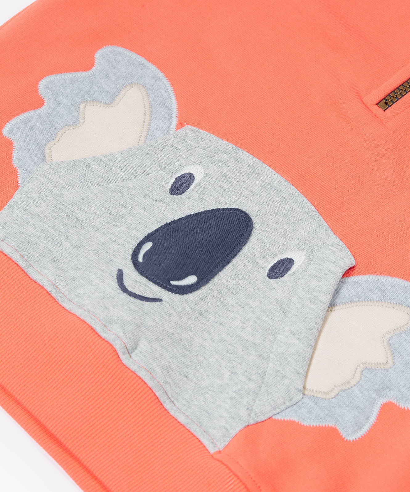 Close up of the Frugi kids koala half zip hoodie showing the appliqué of a grey koala head on coral organic cotton fabric