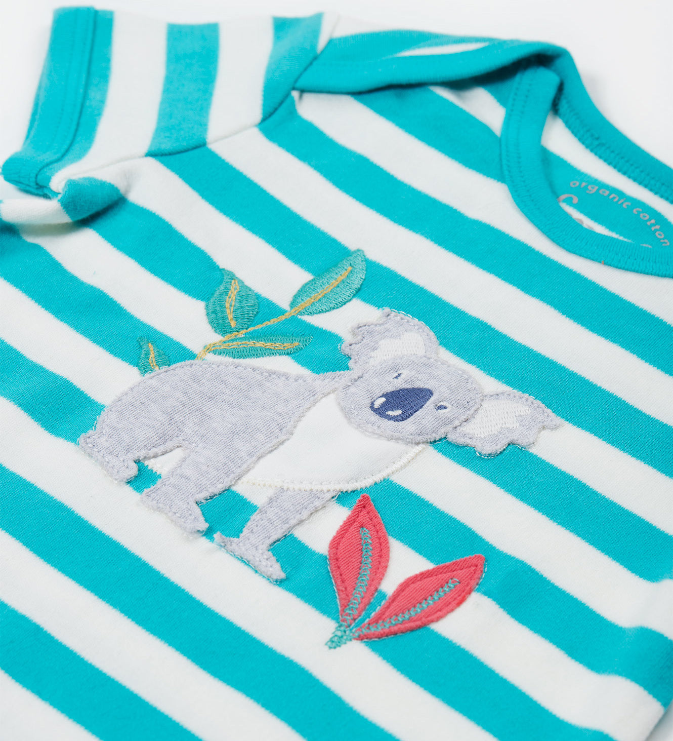 A close up of the Frugi Koala rue romper showing the grey koala applique next to pink leaves and a bamboo shoot on blue and white striped organic cotton fabric