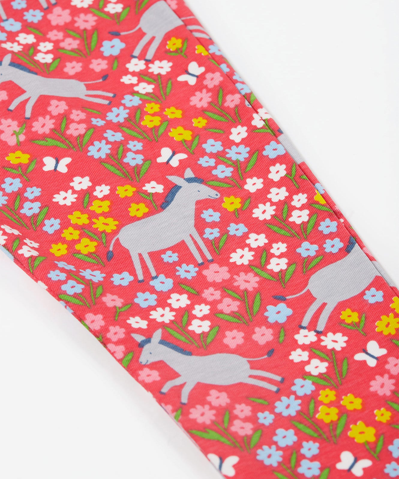 A close up of the Frugi kids donkey drove libby leggings. Showing the grey donkey and multicoloured flower design on light pink organic cotton fabric.