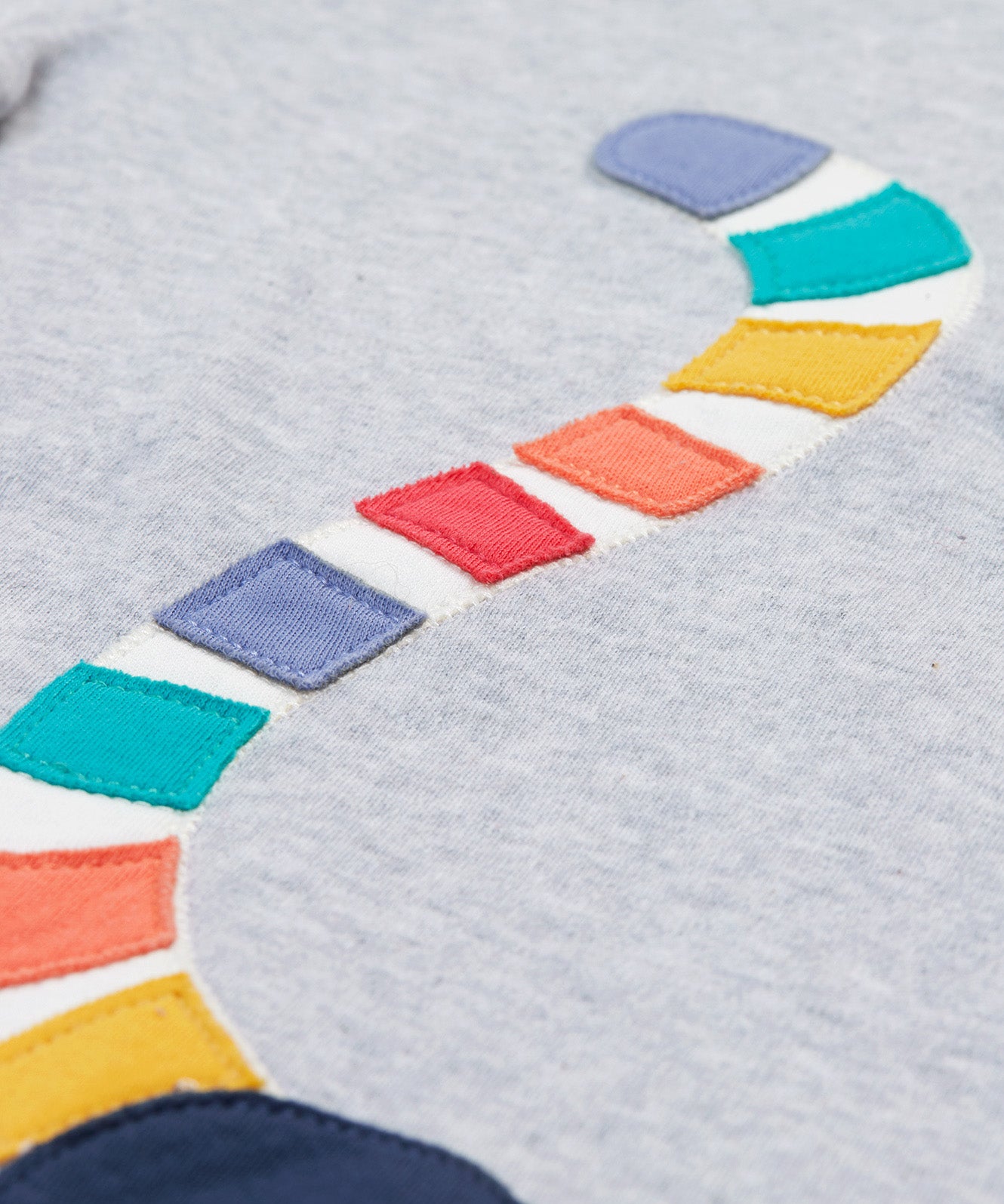 A close up of the Frugi kids grey marl lemur character t- shirt. showing the multicoloured tail of the lemur appliqué on grey marl organic cotton fabric