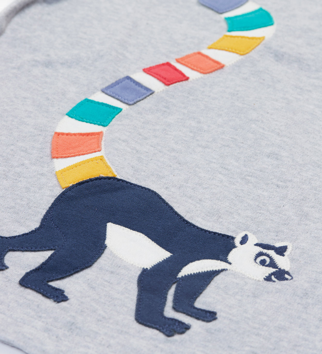 A close up of the Frugi kids grey marl lemur character t- shirt. showing the lemur applique and multicoloured tail on grey marl organic cotton fabric