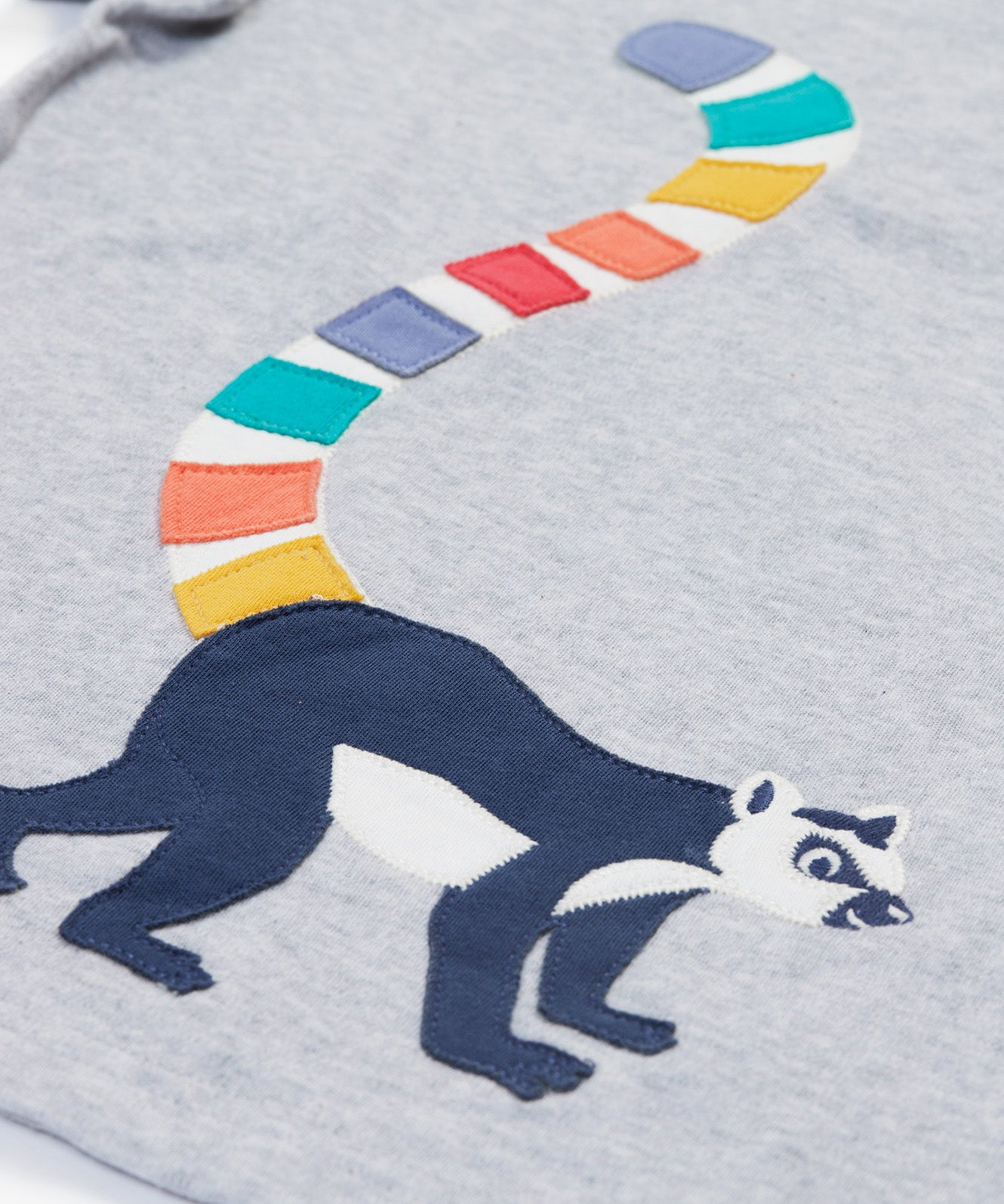 A close up of the Frugi kids grey marl lemur character t- shirt. showing the lemur applique and multicoloured tail on grey marl organic cotton fabric