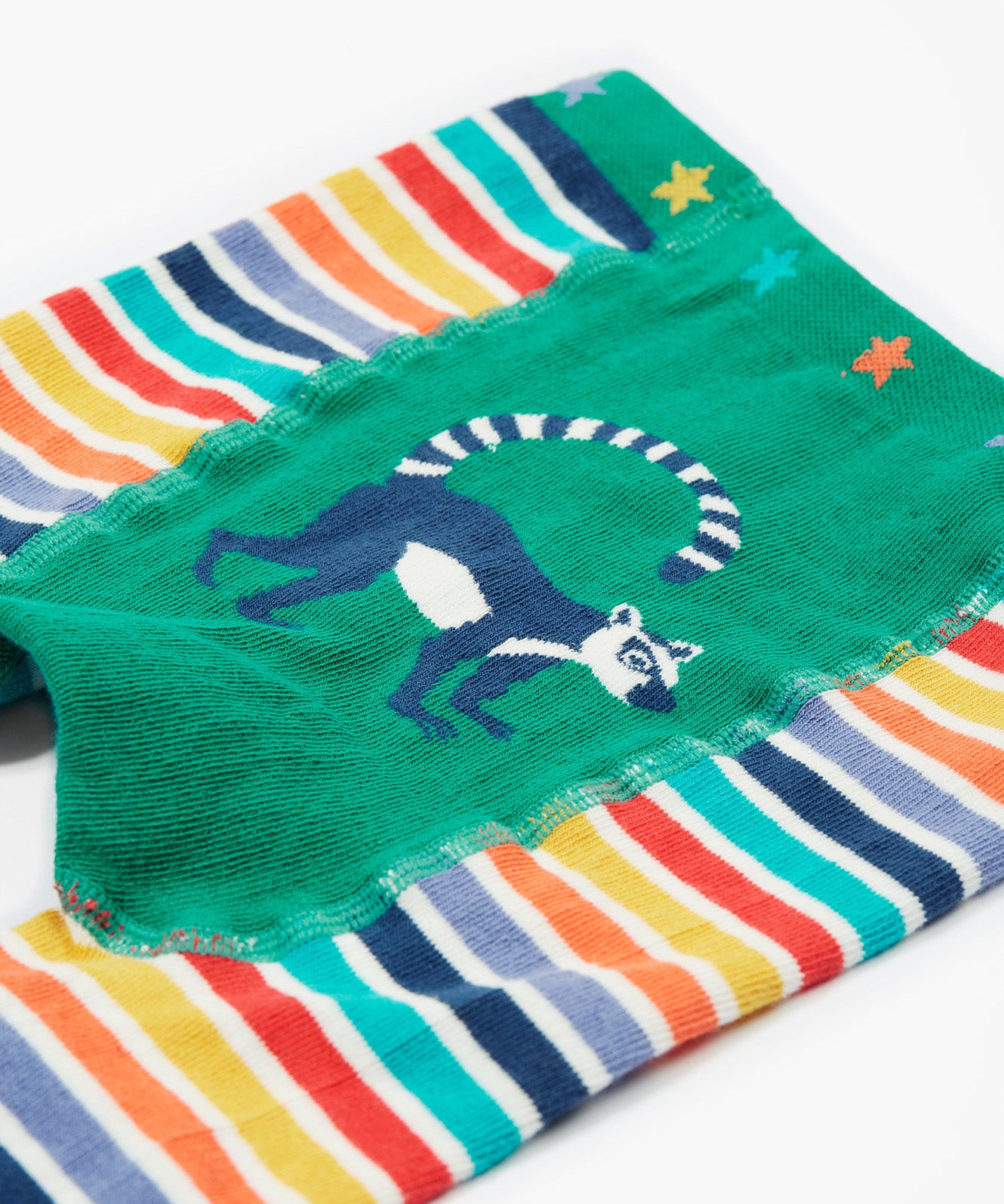 A close up of the Frugi baby lemur knitted leggings showing a navy lemur on a green panel on the front of the leggings on organic soft cotton fabric