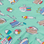 A close up of the Frugi kids lets bake Morwenna skater dress. Showing the different cakes, ice cream, puddings on light green organic cotton fabric