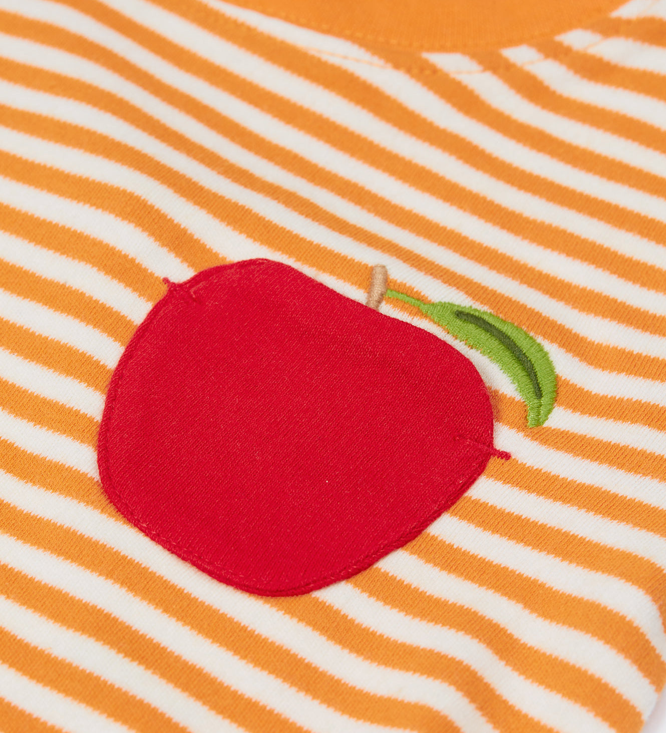 Close up of the the Frugi kids lifeboat stripe, apple t-shirt. Showing the appliqué of a red apple on the front with a green leaf embroidery on orange and white striped organic cotton fabric 