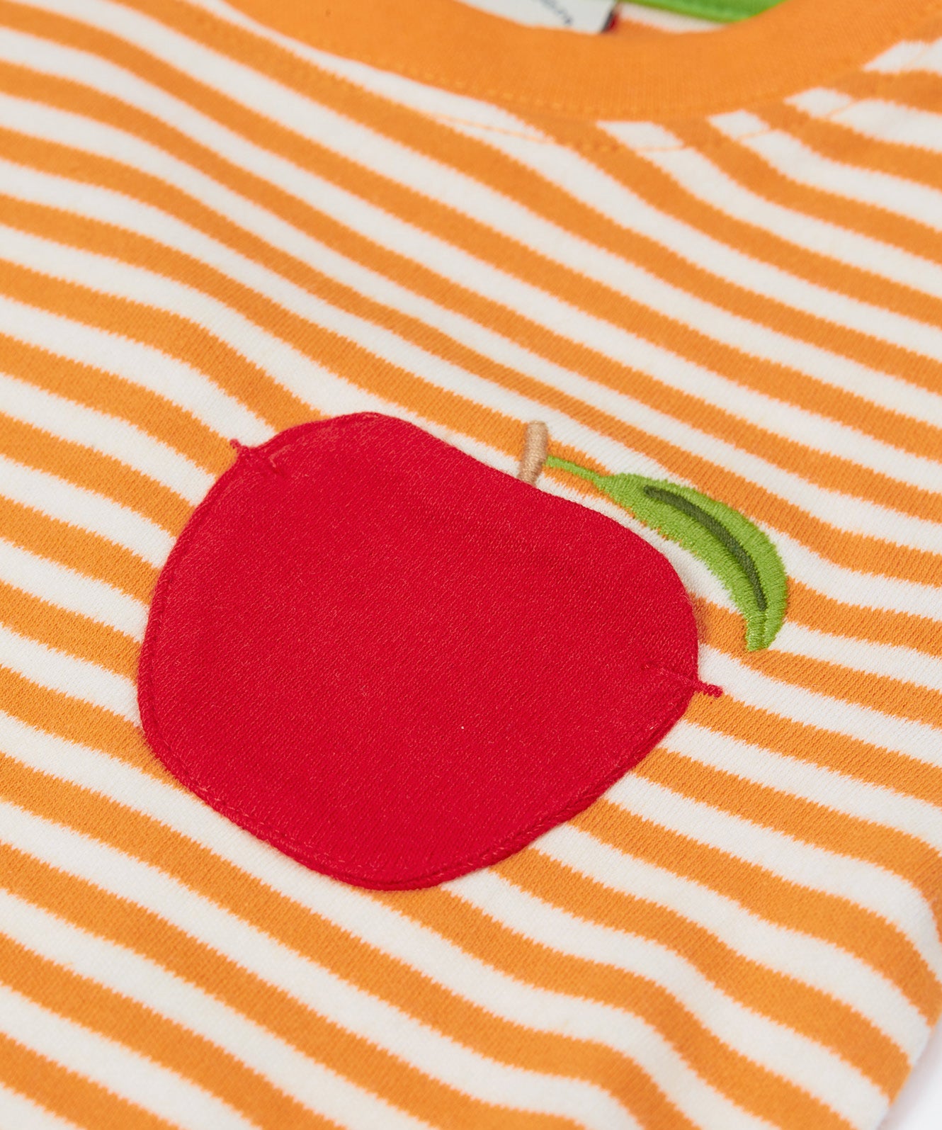 Close up of the the Frugi kids lifeboat stripe, apple t-shirt. Showing the appliqué of a red apple on the front with a green leaf embroidery on orange and white striped organic cotton fabric 