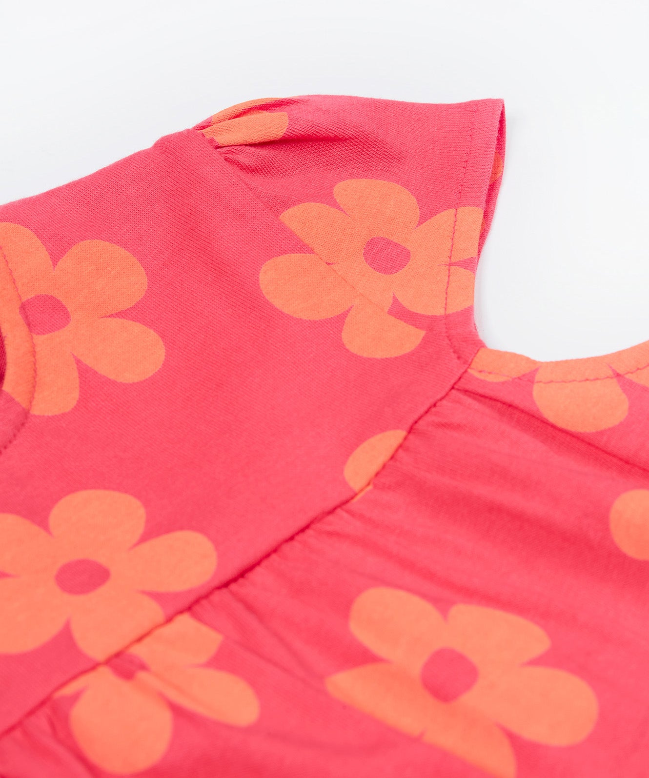 A close up of the Frugi little Lola floral fun / horse dress. Showing the short sleeve detail surrounded with light orange printed flowers on a pink organic cotton fabric