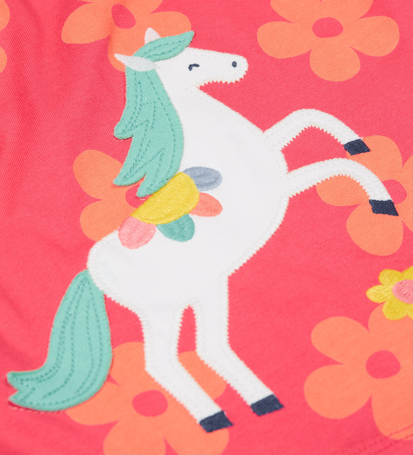 A close up of the Frugi little Lola floral fun / horse dress. Showing the white horse appliqué with light green hair next to appliqué flowers surrounded with light orange printed flowers on a pink organic cotton fabric