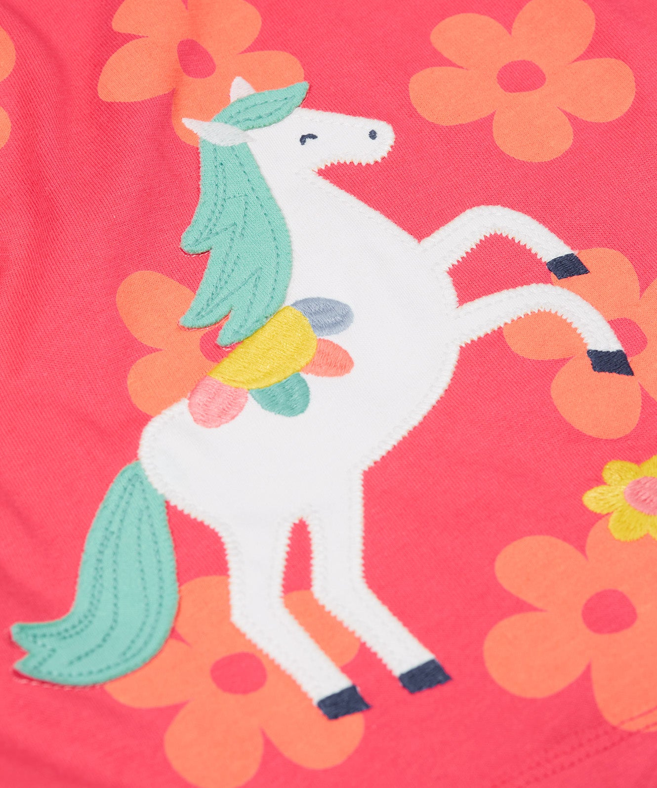 A close up of the Frugi little Lola floral fun / horse dress. Showing the white horse appliqué with light green hair next to appliqué flowers surrounded with light orange printed flowers on a pink organic cotton fabric