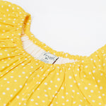 Close up of the Frugi kids lowen flower dress - Showing the slightly elasticated neck trim on yellow with white spots organic cotton fabric