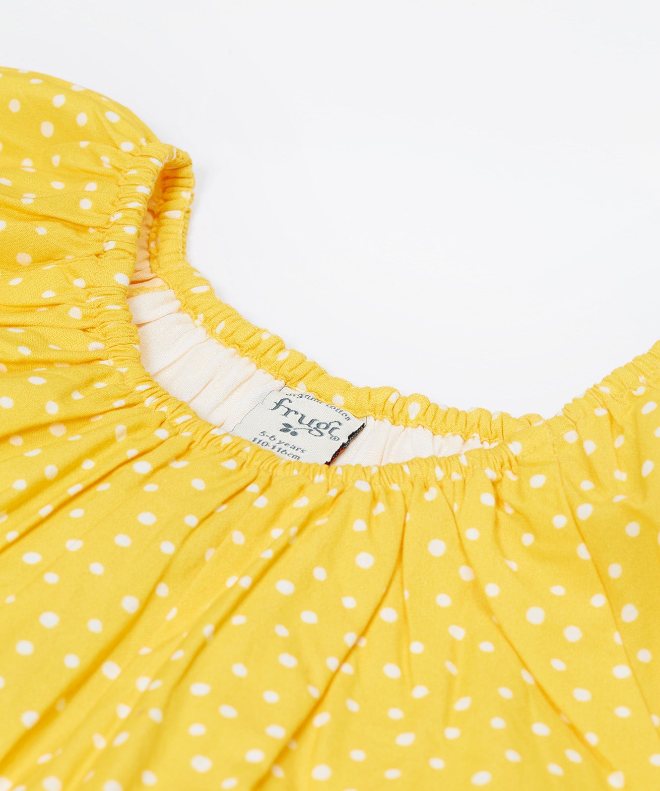 Close up of the Frugi kids lowen flower dress - Showing the slightly elasticated neck trim on yellow with white spots organic cotton fabric