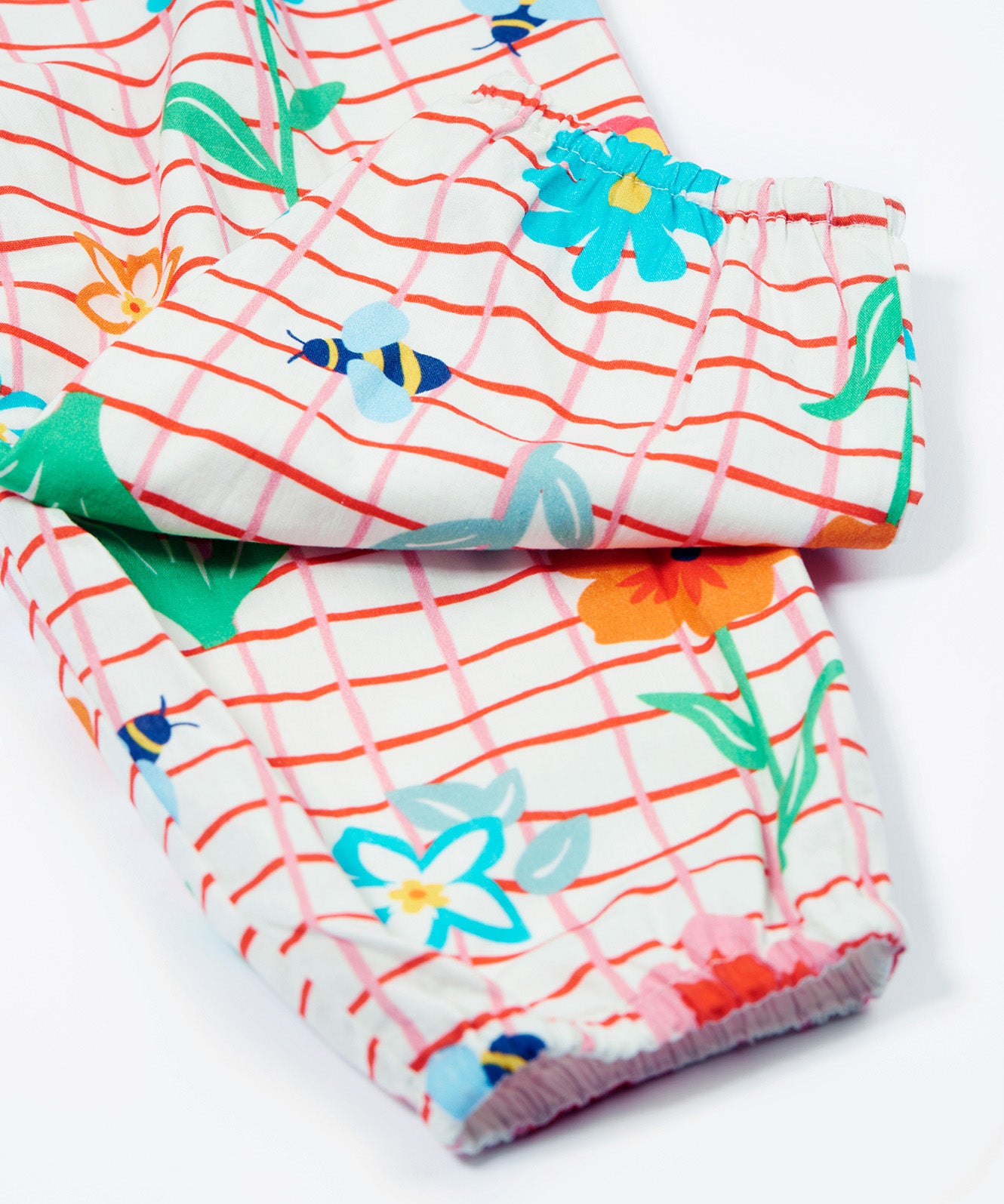 Close up of the Frugi baby Lula paint a floral playsuit. Showing the elasticated leg cuff detail on white and red check organic cotton fabric