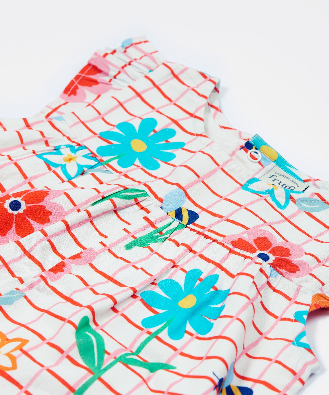 Close up of the Frugi baby Lula paint a floral playsuit. Showing the yellow bees and different coloured flowers on white and red check organic cotton fabric