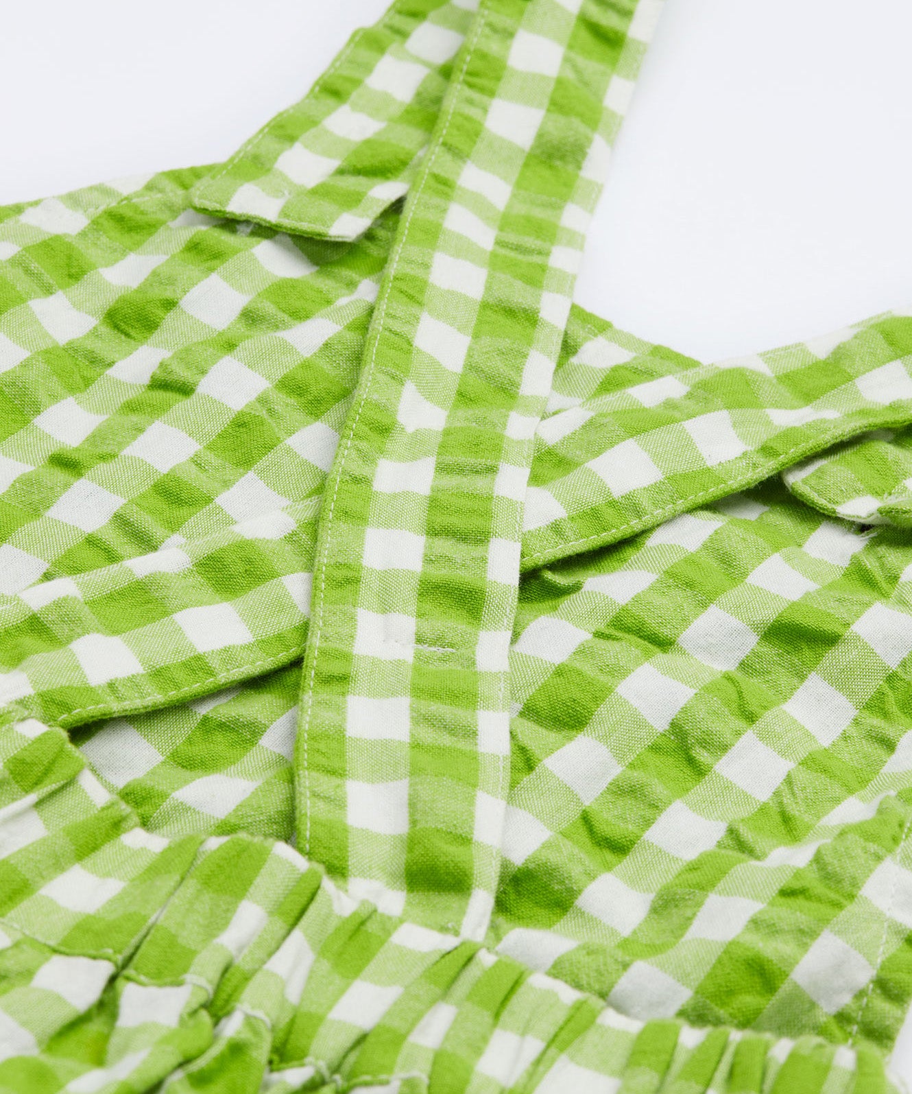 Close up of the Frugi kids macaw ginham, veg culotte dungarees. Showing criss cross shoulder strap detail on green and white gingham organic cotton fabric