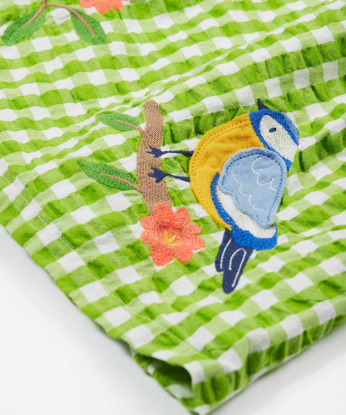 Close up of the Frugi kids macaw gingam birds dress. Showing the bird applique on a green and white gingham organic cotton fabric.