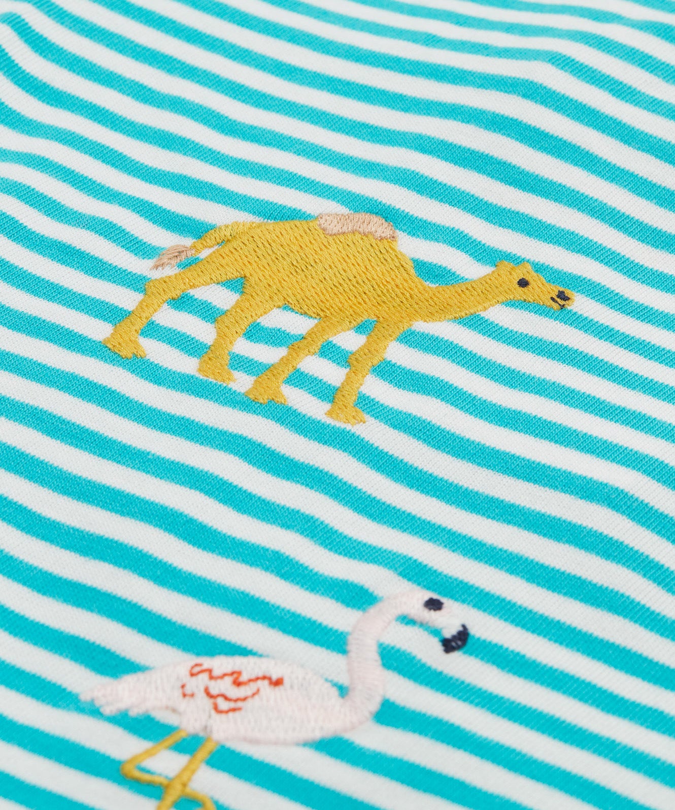 A close up of the Frugi kids moss stripe wildlife t-shirt. Showing the camel applique detail next to the pelican applique on blue and white stripe organic cotton fabric.