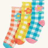 Frugi kids Freya frilled gingahm socks - GOTS organic cotton kids socks with a frilled cuff. Features a blue gingham with pink daisy sock, a yellow gingham with light orange daisy sock and a light orange gingham and blue daisy sock. 