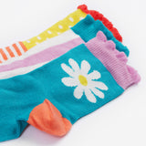 A close up of the Frugi kids Freya frilled let's create 3 pack frilled socks - Showing the  striped socks with a light blue cuff, a light blue sock and white daisy design and a spotted/striped sock on organic cotton fabric