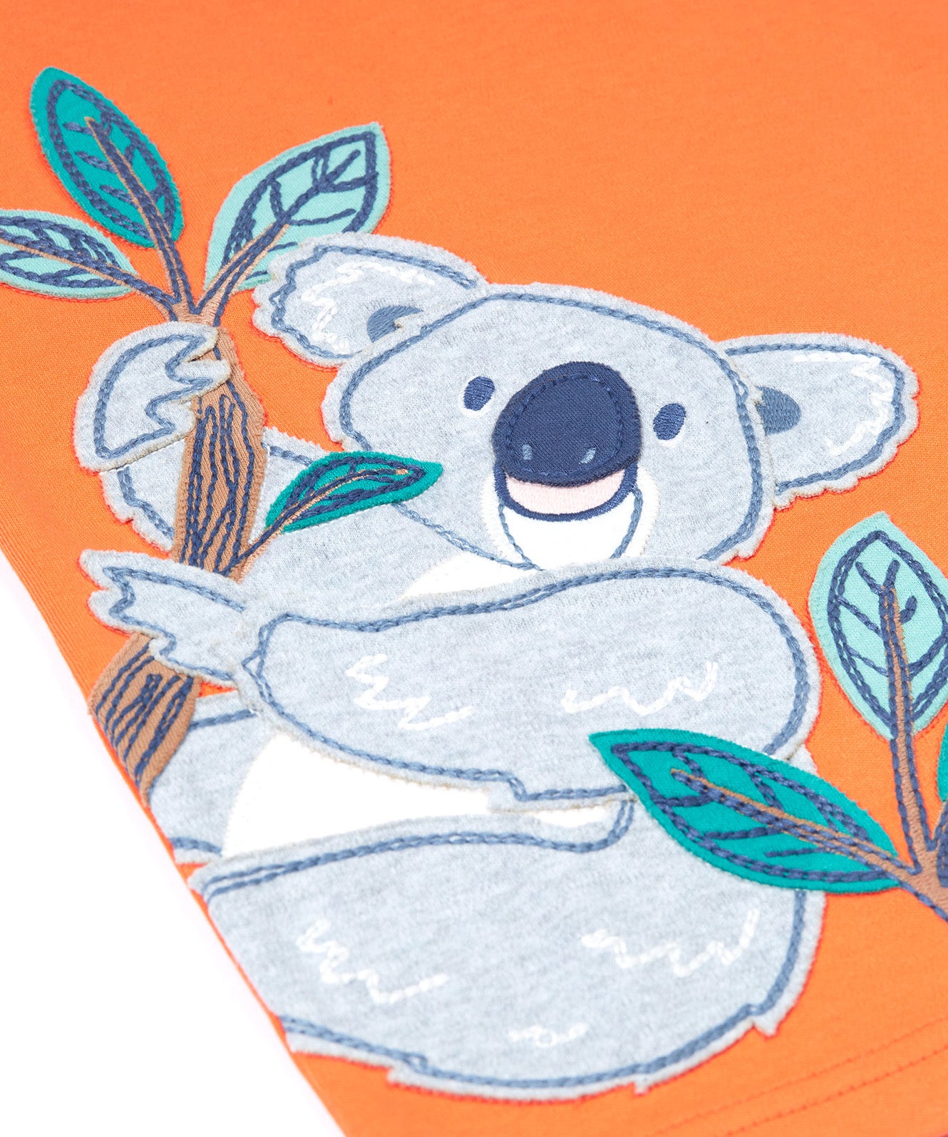 Close up of the Frugi kids orange koala t-shirt. Showing the grey koala applique hanging on embroidered bamboo shoots on light orange organic fabric