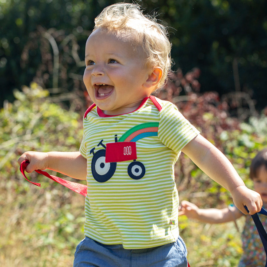 Child running around outside wearing the Frugi Pear green Striped Tractor Bobster Applique T-Shirt 