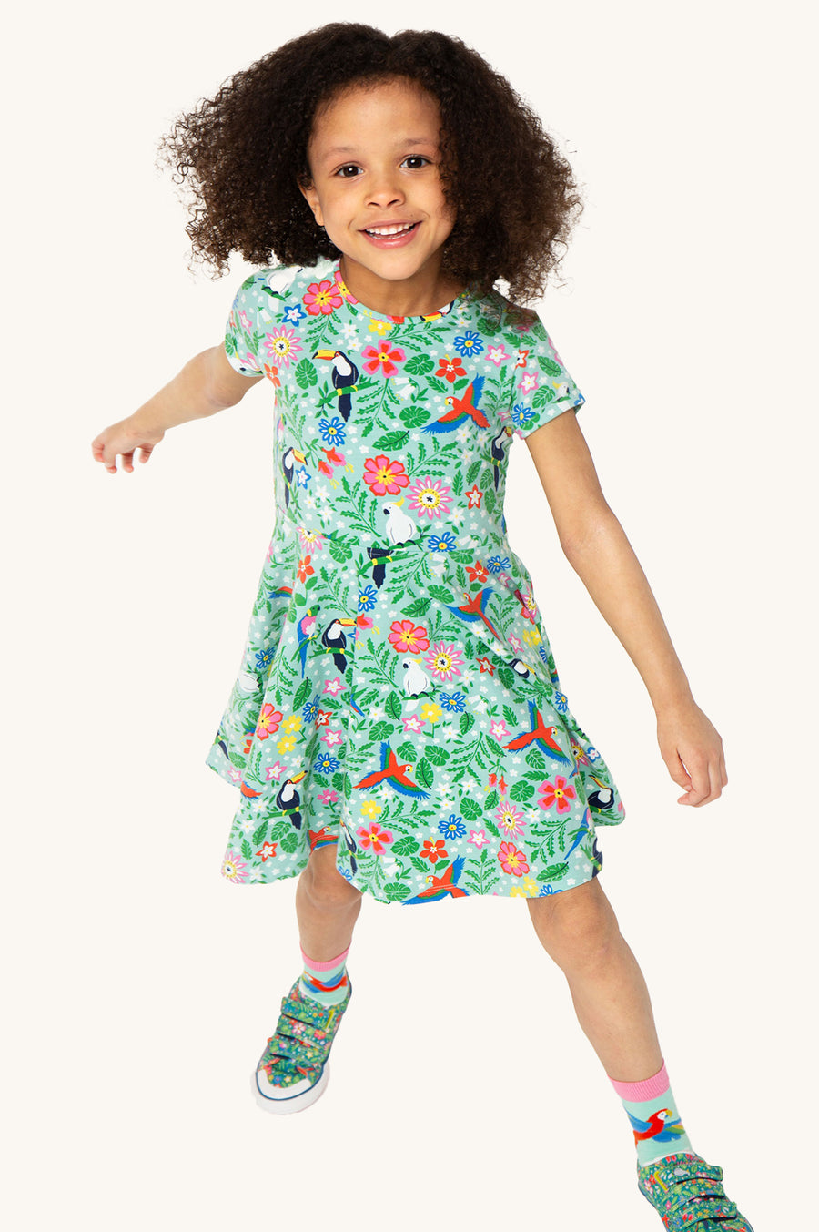 A child looking down at the Frugi Children's Organic Cotton Spring Skater Dress - Tropical Birds. A beautiful tropical bird and flower print on a twirly short sleeve skater dress they are wearing