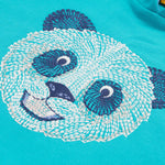 A close up of the Frugi kids oversized blue panda hoodie. Showing the white and navy panda embroidery on the front on blue organic cotton fabric