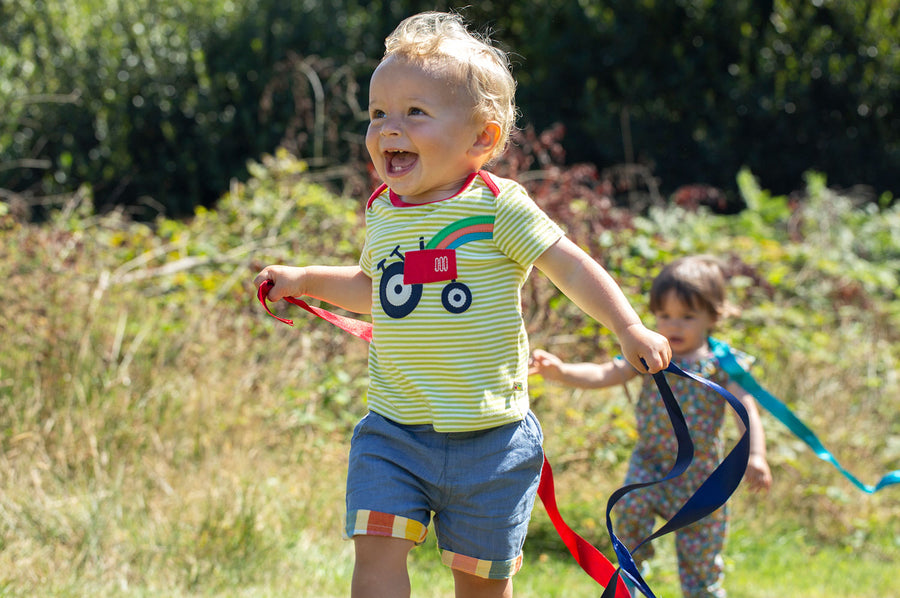 Child running around outside wearing the Frugi Pear green Striped Tractor Bobster Applique T-Shirt 