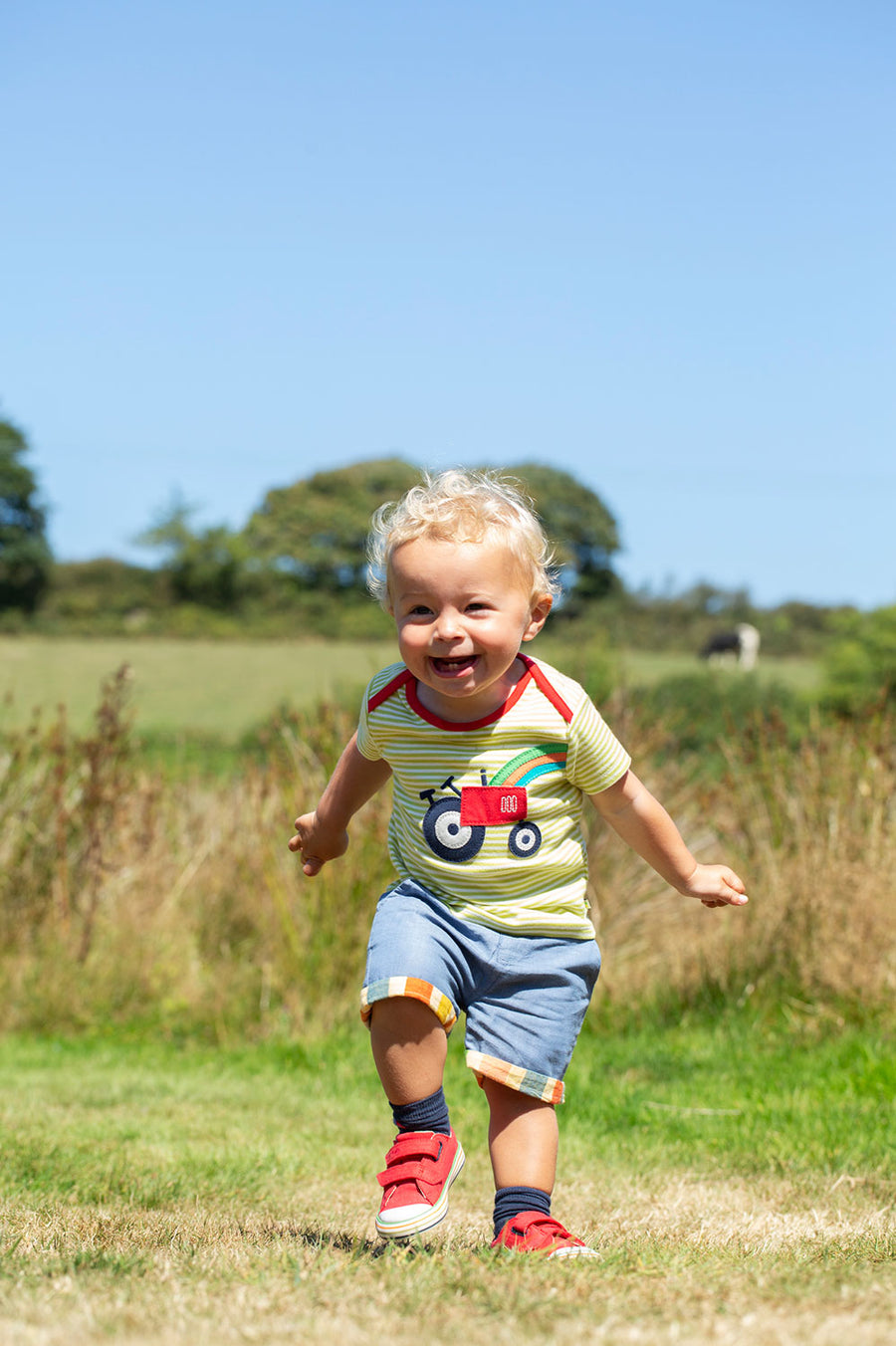 Child running around outside wearing the Frugi Pear green Striped Tractor Bobster Applique T-Shirt 