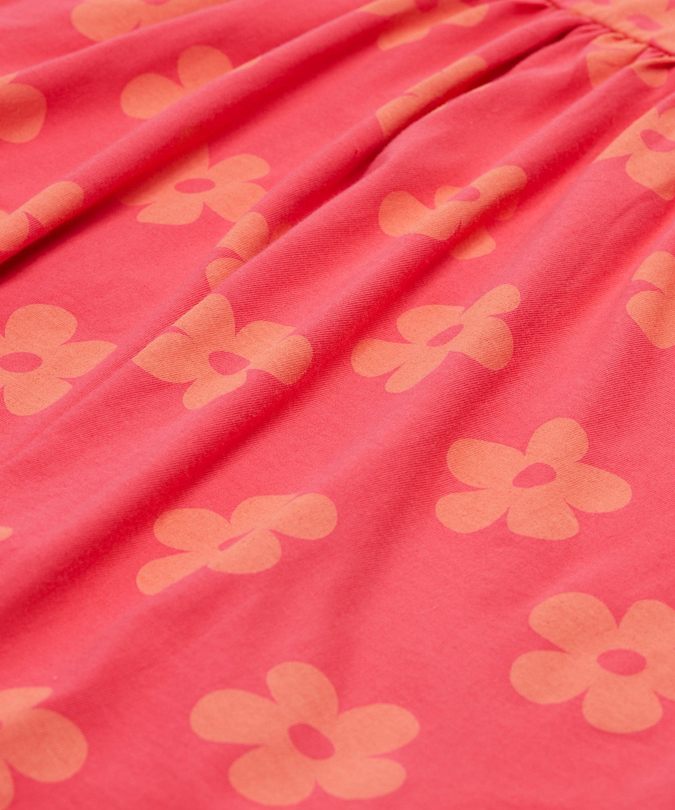 A close up of the Frugi kids summer flamingo / flower dress. Showing the detail of the coral flowers print on pink organic cotton fabric