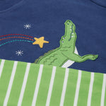 A close up of the Frugi kids Porth crocodile pyjama set showing the appliqué of a star and green crocodile with a star embroidery on the top and the green striped shorts on organic cotton fabric