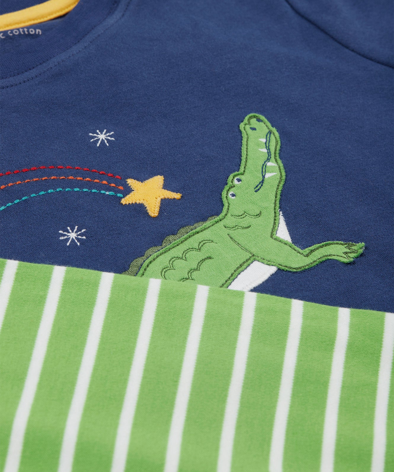 A close up of the Frugi kids Porth crocodile pyjama set showing the appliqué of a star and green crocodile with a star embroidery on the top and the green striped shorts on organic cotton fabric