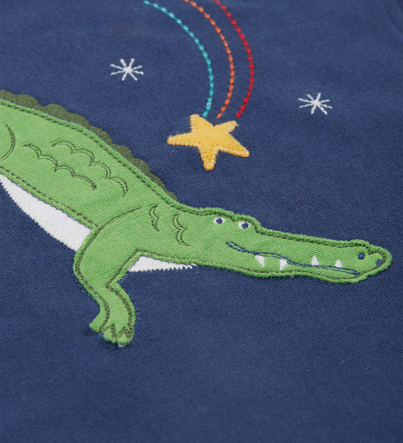 A close up of the Frugi kids Porth crocodile pyjama set showing the appliqué of a star and green crocodile with a star embroidery on a navy organic cotton fabric