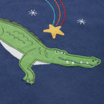 A close up of the Frugi kids Porth crocodile pyjama set showing the appliqué of a star and green crocodile with a star embroidery on a navy organic cotton fabric