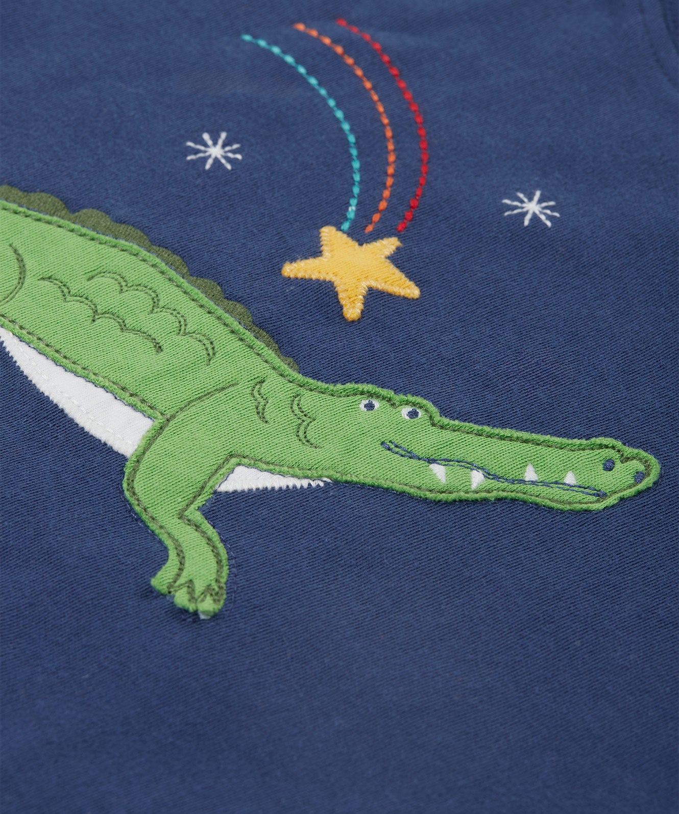 A close up of the Frugi kids Porth crocodile pyjama set showing the appliqué of a star and green crocodile with a star embroidery on a navy organic cotton fabric