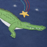 A close up of the Frugi kids Porth crocodile pyjama set showing the appliqué of a star and green crocodile with a star embroidery on a navy organic cotton fabric