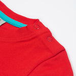 Close up of the Frugi kids strawberry quokka tshirt. Showing the popper fasteners on the shoulder for easy fitting with a light blue trim on inside neck on red organic cotton fabric