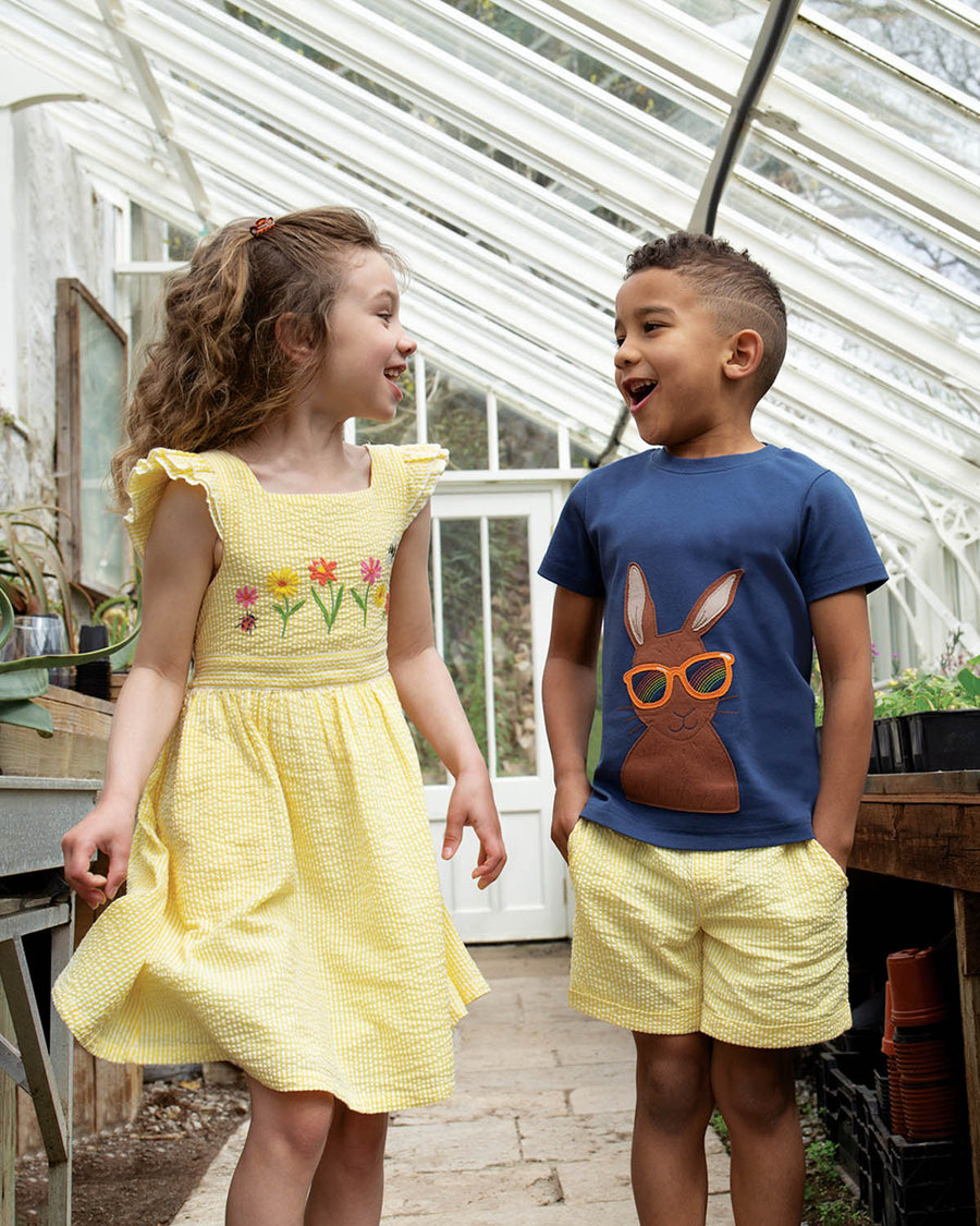 A closer view of the Frugi Carsen Applique T-Shirt - Hare. A deep navy blue GOTS organic cotton t-shirt with a brown hare wearing yellow sunglasses with a rainbow reflection in the lens