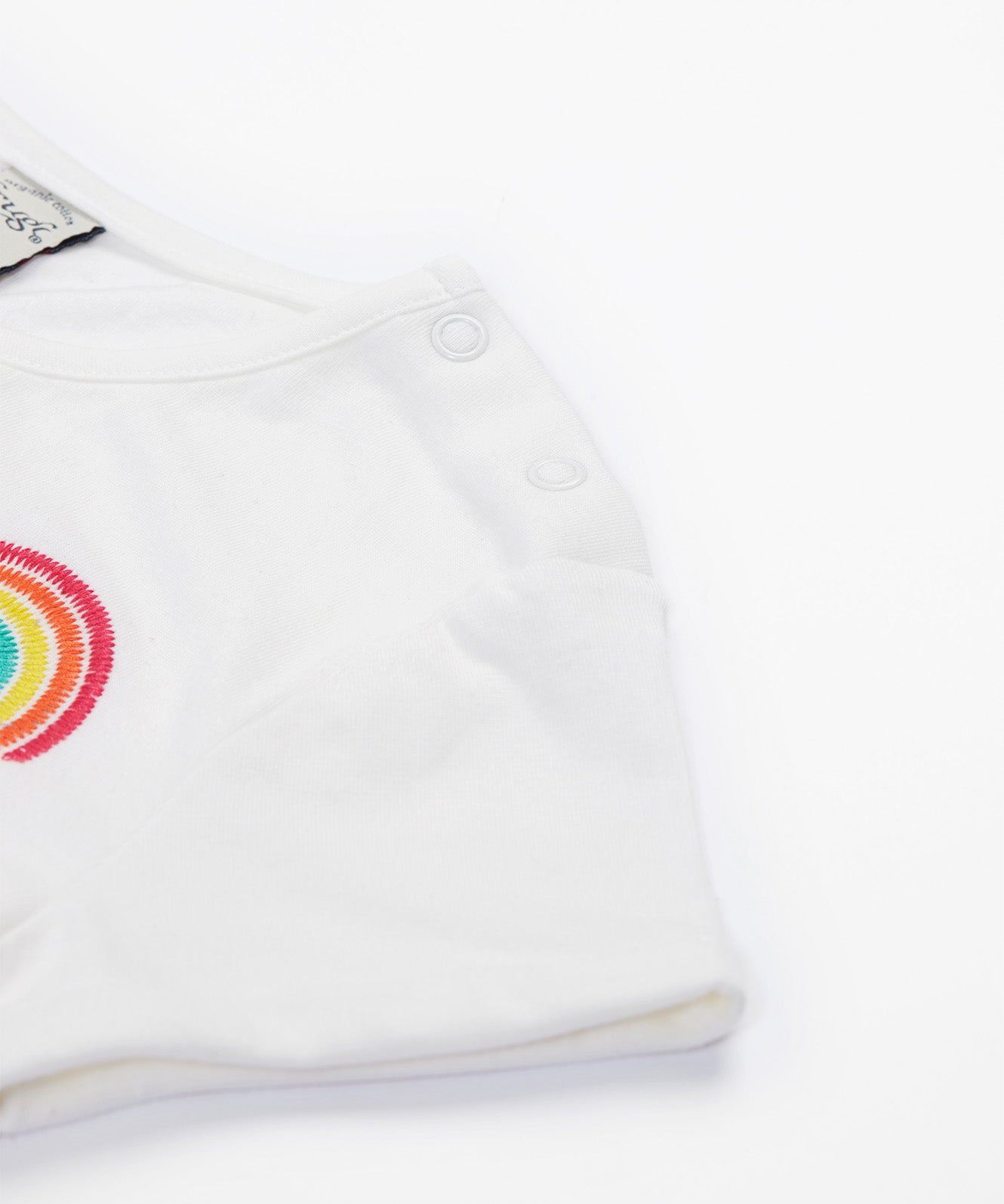 Close up of the Frugi kids jersey rainbow dress - showing a rainbow embroidery and shoulder popper fasteners for easy fitting on white organic cotton fabric