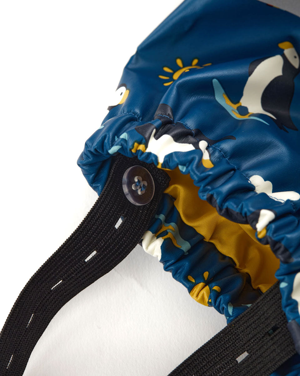 Close up of the adjustable button straps on the Frugi puffin print waterproof suit on a white background