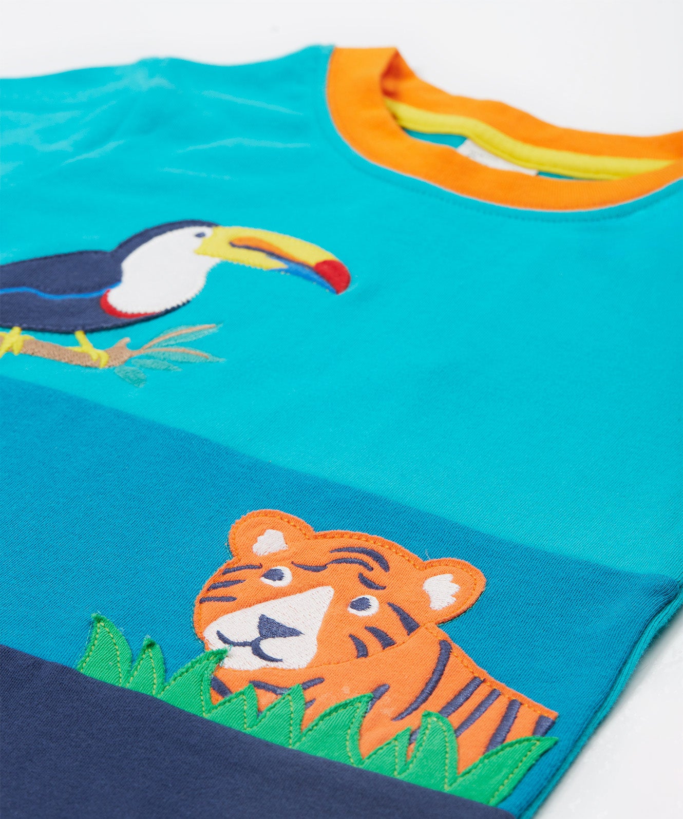 A close up of the Frugi sea, land, canopy short sleeve -shirt. Showing the orange neck trim and the toucan and  tiger appliqué stitched on a blue organic cotton fabric