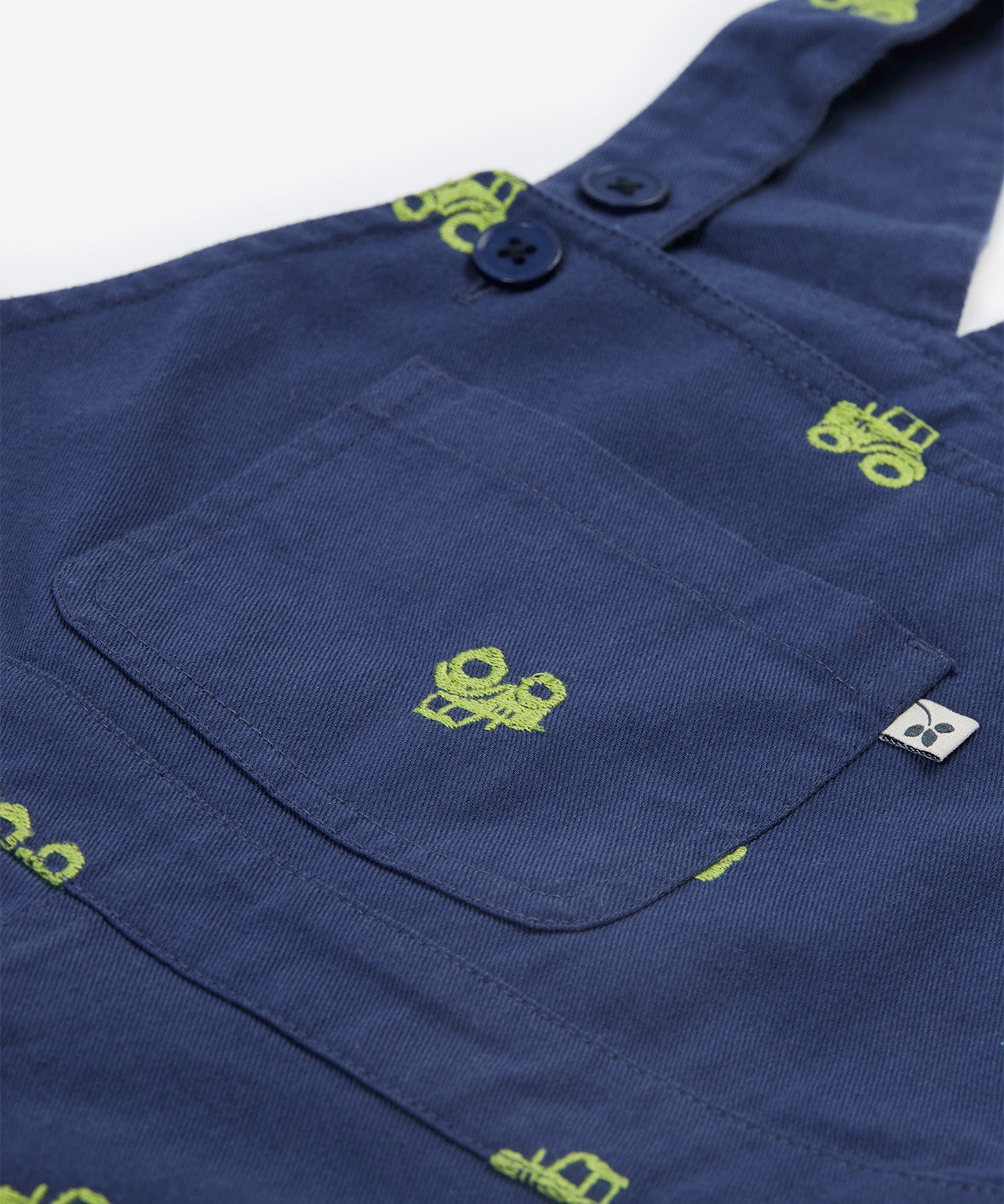 Close up of the Frugi baby short navy tractor dungarees. Showing the front pocket detail and green tractor embroidery on navy organic cotton fabric.