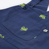 Close up of the Frugi baby short navy tractor dungarees. Showing the front pocket detail and green tractor embroidery on navy organic cotton fabric.