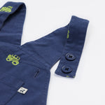 Close up of the Frugi baby short navy tractor dungarees. Showing the button fastener detail and green tractor embroidery on navy organic cotton fabric.