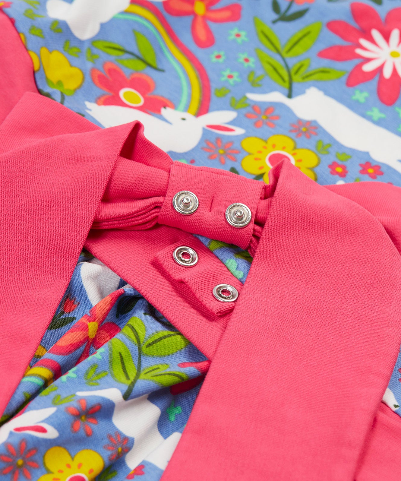 A close up of the Frugi kids bunny bounce skater dress. Showing the pink bow waist band popper detail pastel purple organic cotton fabric