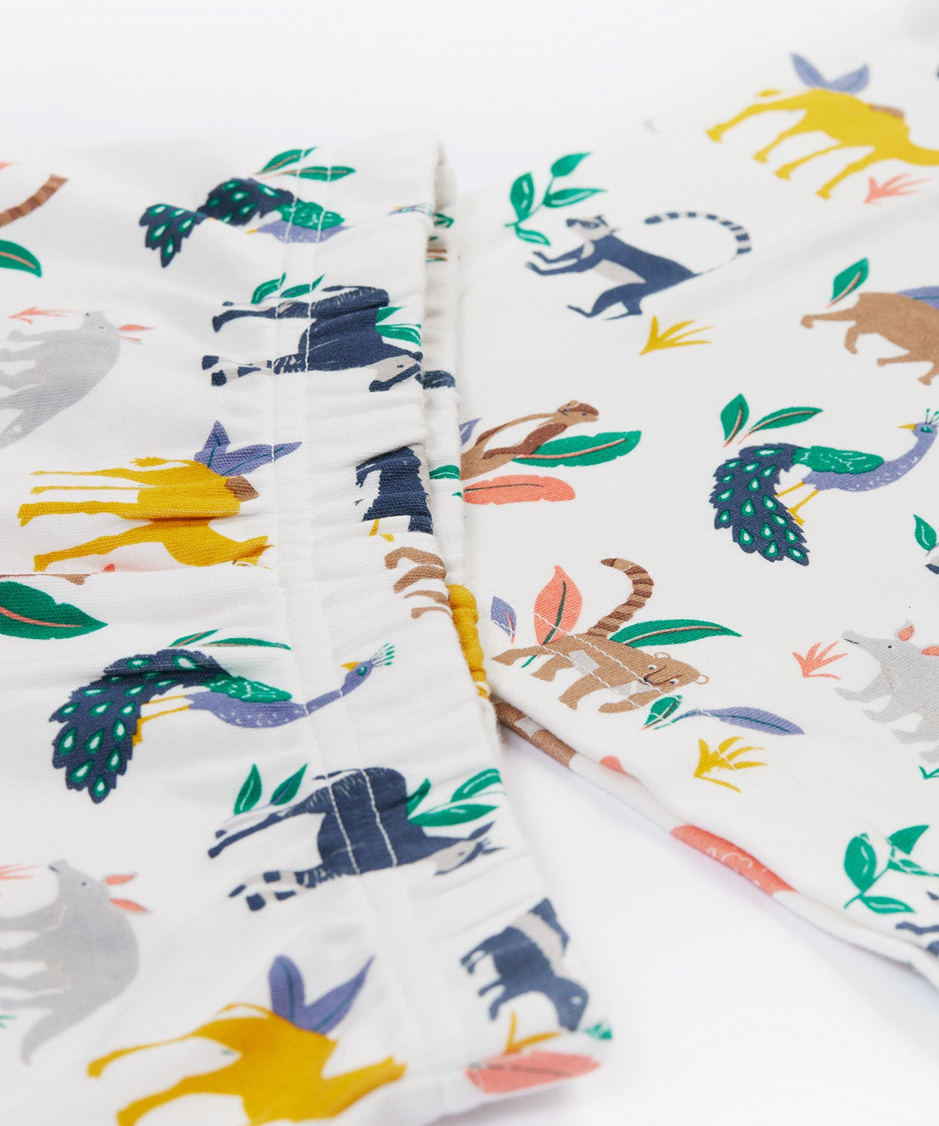 A close up of the Frugi kids snooze wildlife pyjama set showing the prints of different wild animals and the elastic waist band on the shorts on white organic cotton fabric