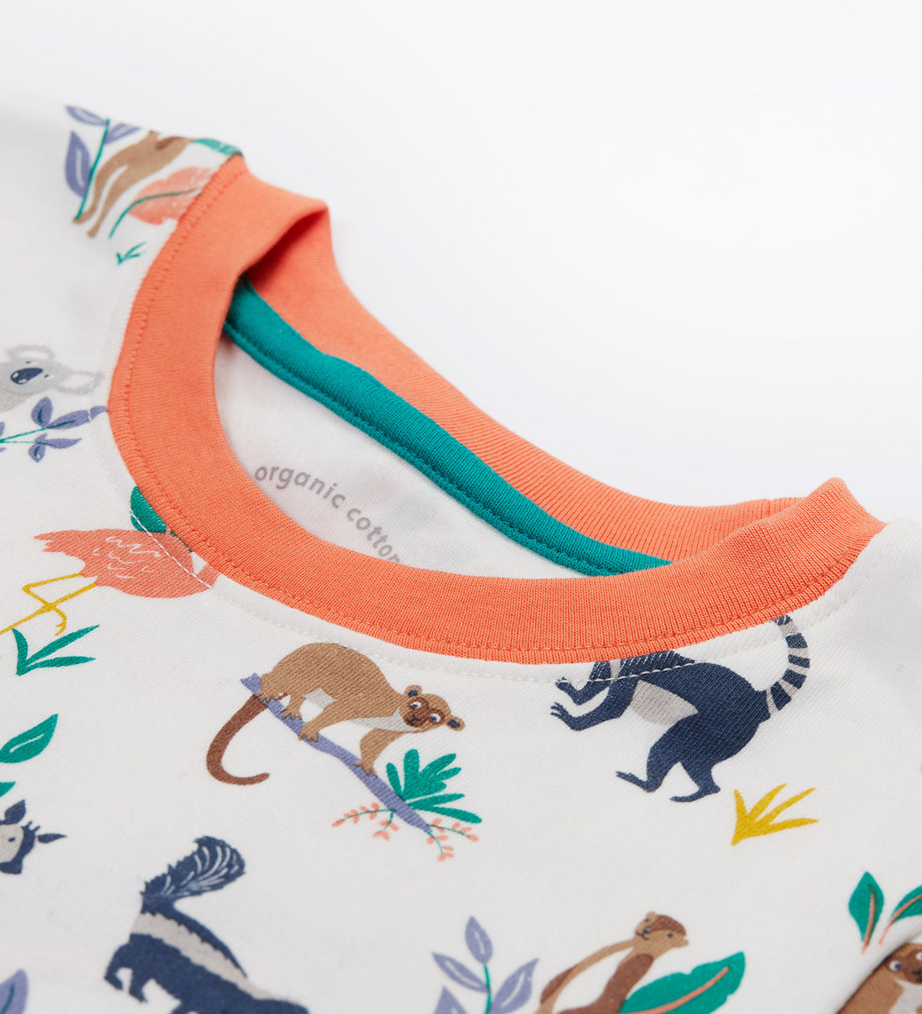 A close up of the Frugi kids snooze wildlife pyjama set showing the prints of different wild animals and orange neck trim on white organic cotton fabric