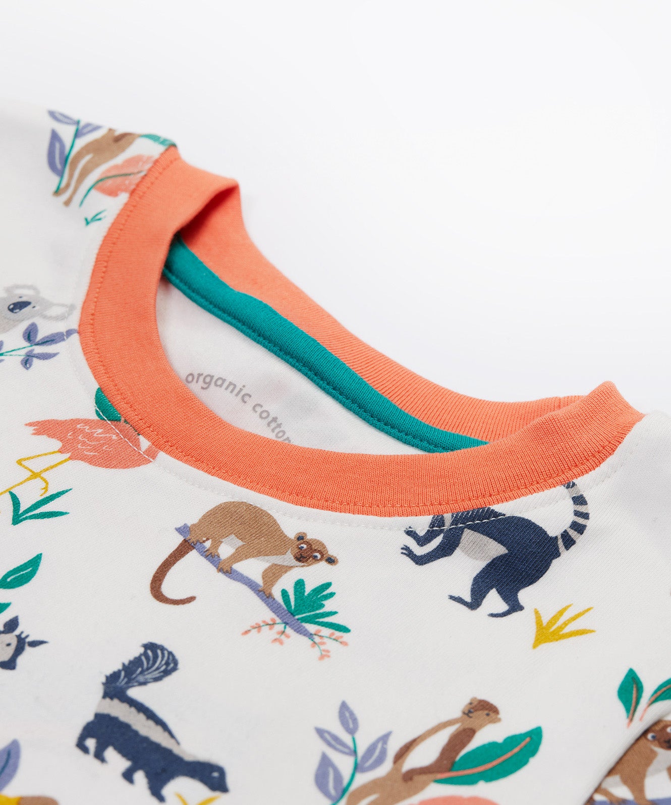 A close up of the Frugi kids snooze wildlife pyjama set showing the prints of different wild animals and orange neck trim on white organic cotton fabric