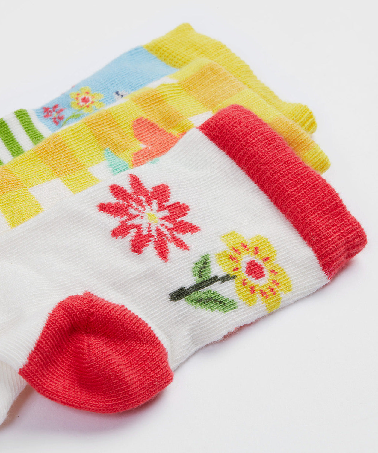 A close up of the Frugi kids spring 3 pack socks - GOTS organic kids socks which features a white sock with a pink trim and flowers design. A yellow gingham sock with a flower design and a green striped sock with a rabbit design.