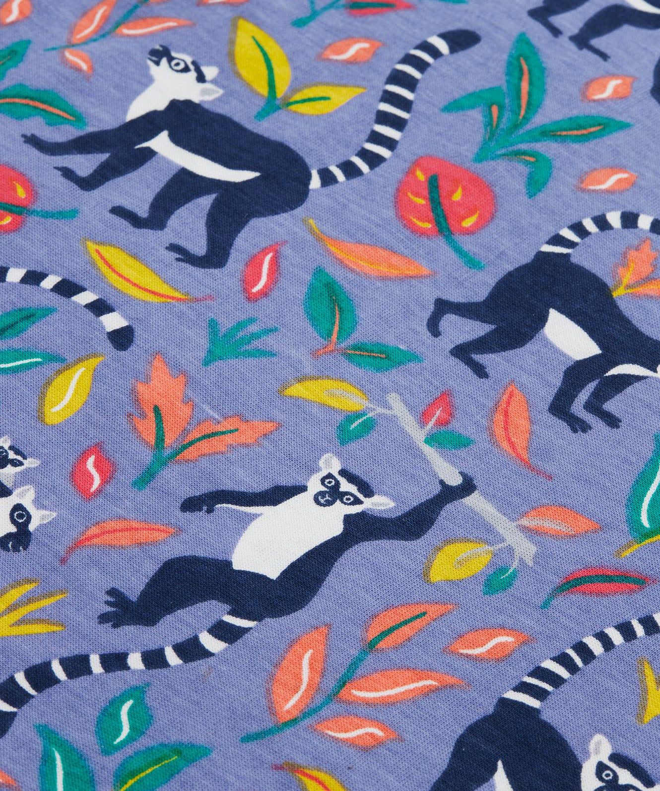 Close up of the Frugi kids summer holiday dress lemur laughs. Showing the lemurs on the bottom half surrounded by different coloured leaves  on purple organic cotton fabric