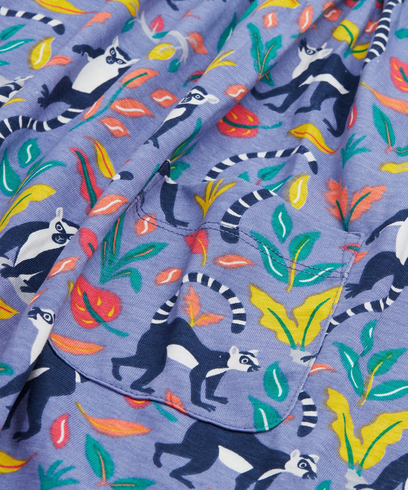 Close up of the Frugi kids summer holiday dress lemur laughs. Showing the lemurs on the bottom half surrounded by different coloured leaves   and front pocket detail on purple organic cotton fabric